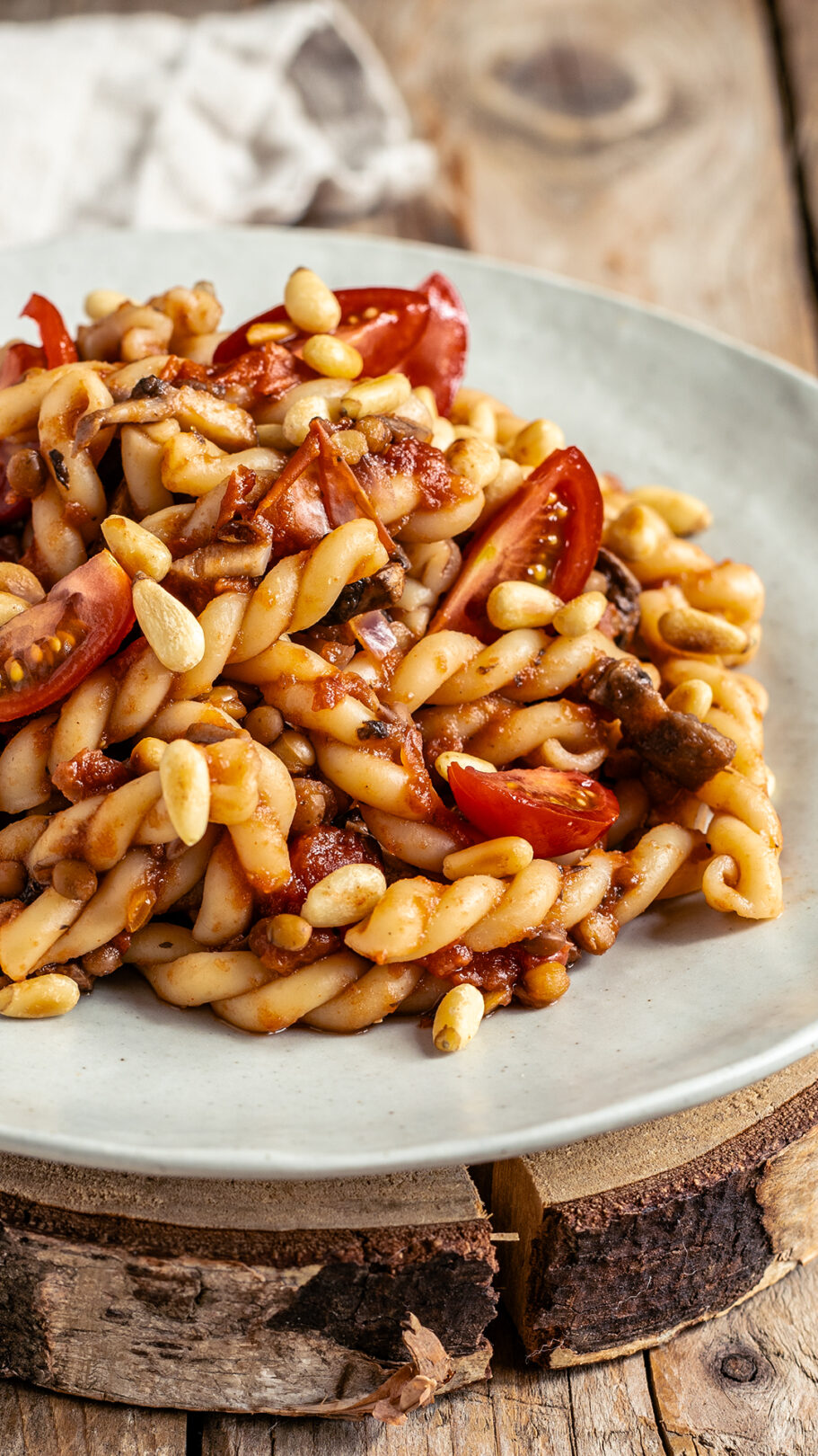 Eine Nahaufnahme eine Pastatellers mit einer köstlichen Linsen Pilz Bolognese, ein paar frischen Tomaten und gerösteten Pinienkernen darauf.