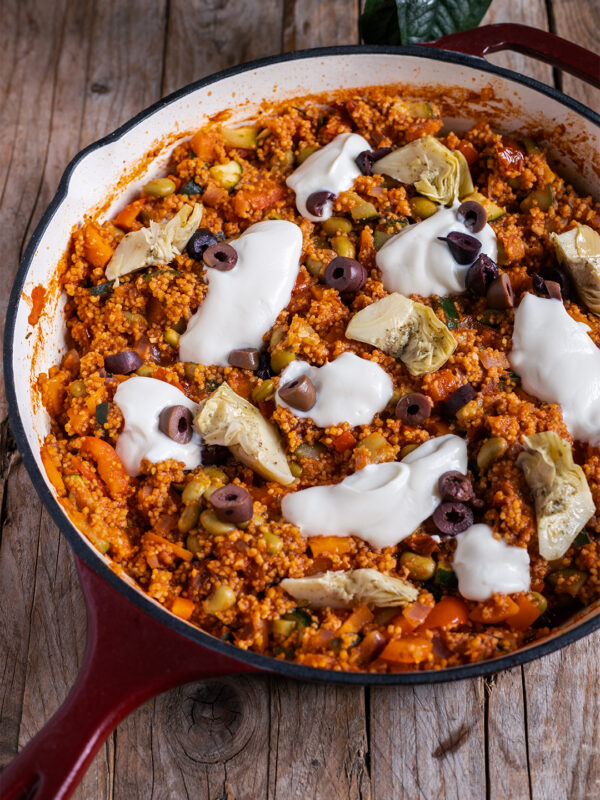 Vegane Couscous-Pfanne mit Gemüse, Edamame, Oliven und Artischocken in einer weiten Pfanne