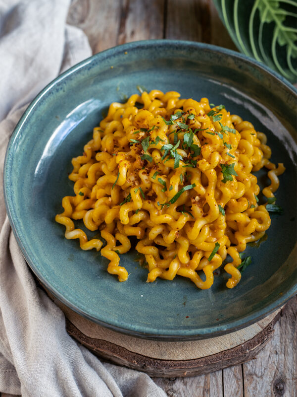 Eine Portion herrliche orangene Kürbispasta in einer hübschen grünen Schale. Garniert mit frischem Koriander und Sonnenblumenkernen.