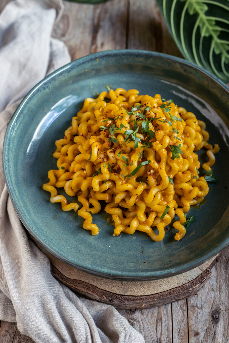 Eine Portion herrliche orangene Kürbispasta in einer hübschen grünen Schale. Garniert mit frischem Koriander und Sonnenblumenkernen.